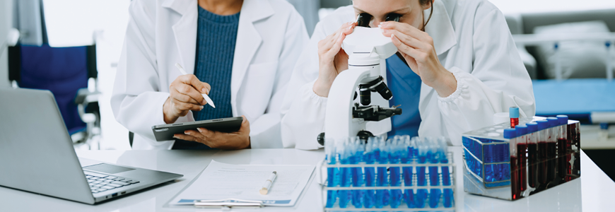 Physician researchers in lab with one looking in a microscope