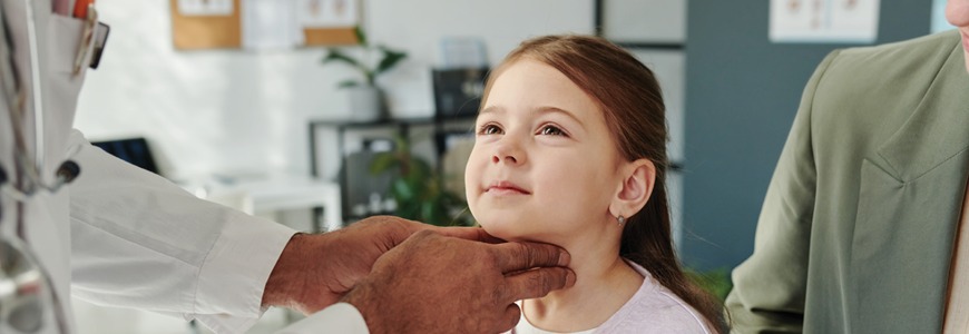Hands of mature male doctor on neck of cute little patient with soft toy during examination of thyroid at medical consultation in clinics
