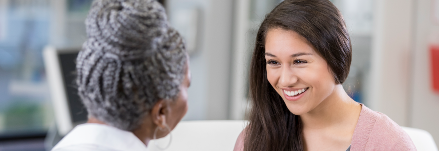 Teenage girl has a smile on her face as she talks with a female gynecologist.