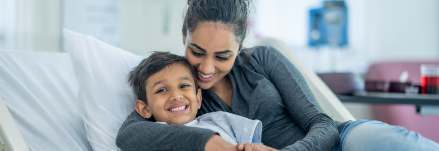 Young boy in hospital bed being hugged by his mom