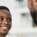 A young boy of African decent sits up on an exam table as he talks with his doctor